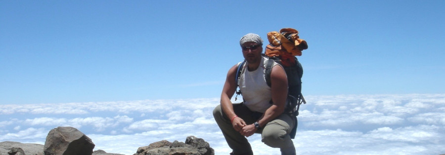 Me posing with backpack on, clouds below in the distant, as I climb Mt Kilimanjaro